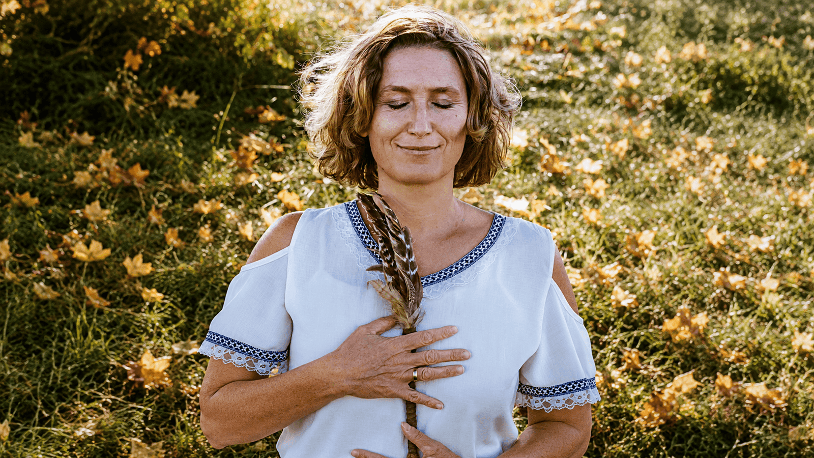 Claudia draußen im Herbstlicht, Augen geschlossen, eine Feder am Herzen