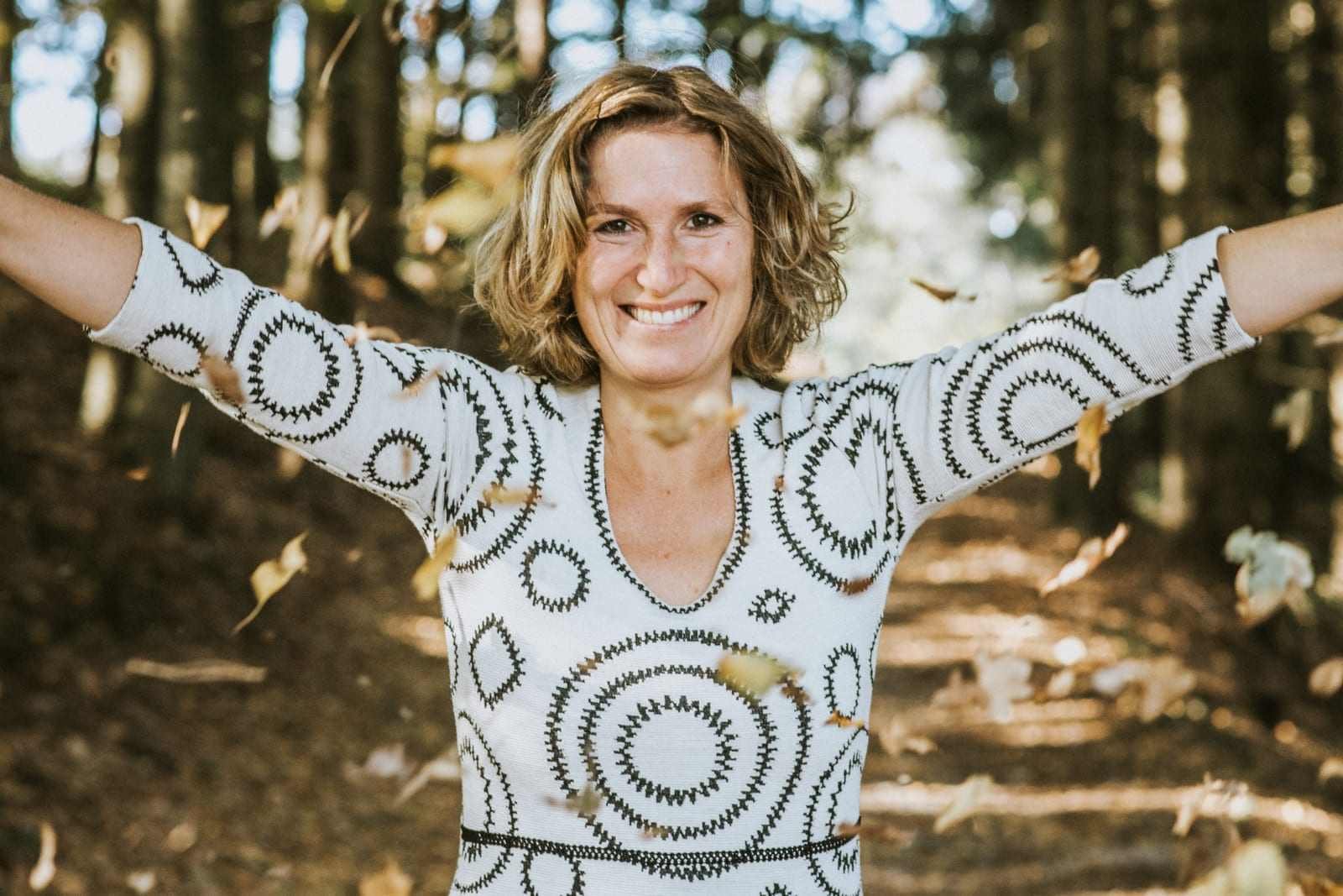 Claudia Reisecker zwischen fallendem Herbstlaub, Arme weit geöffnet